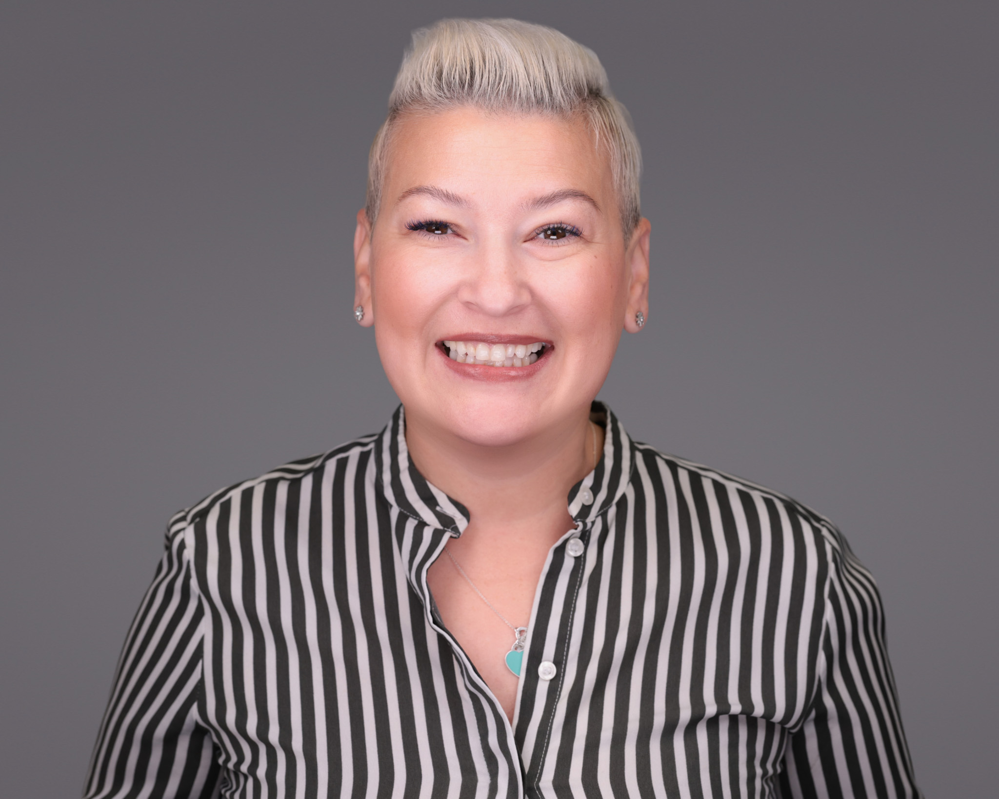 Smiling woman with short gray hair in a striped shirt, studio headshot against a dark gray backdrop