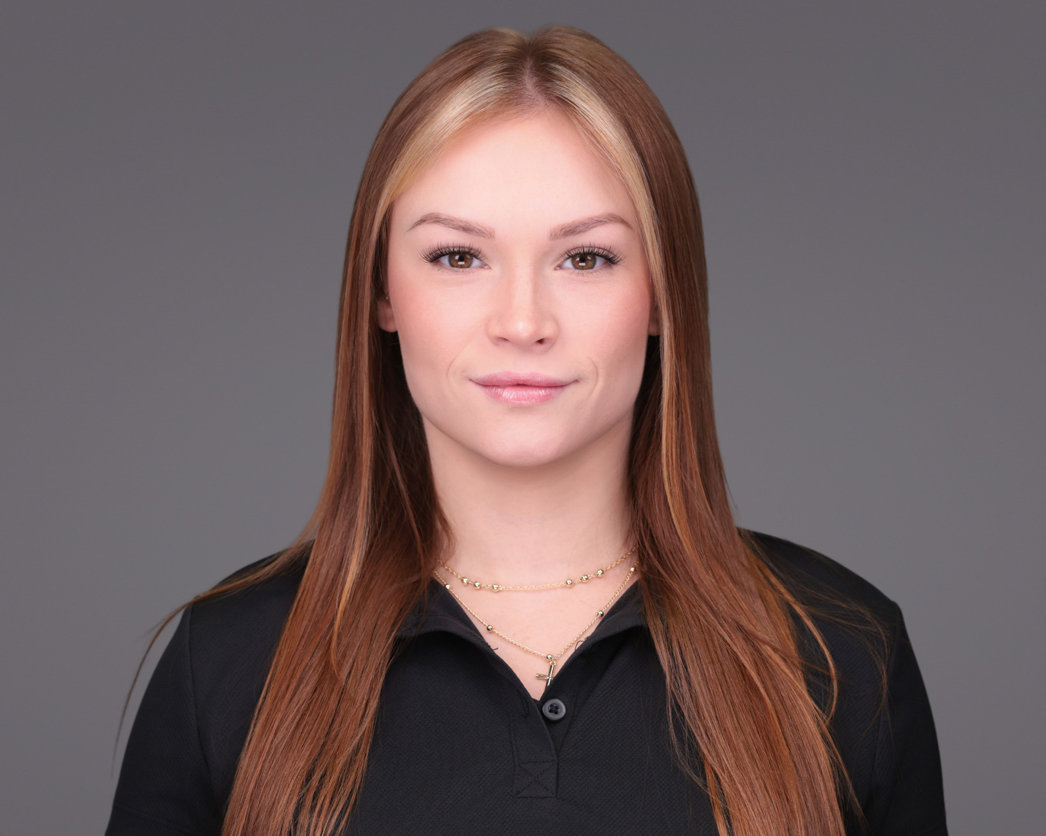Woman with long auburn hair in a black top, studio headshot against a dark gray backdrop