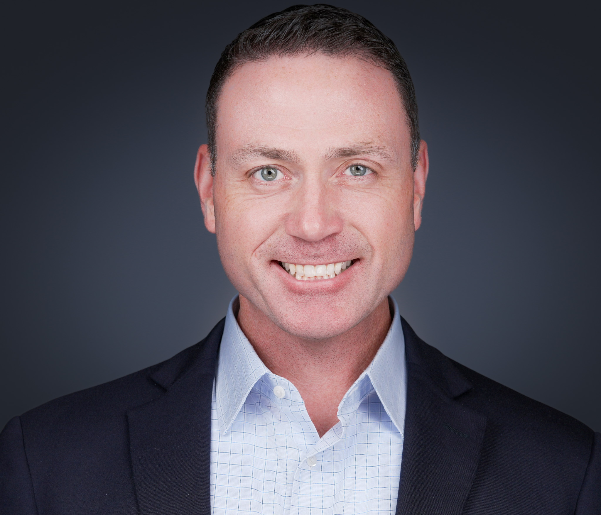 Close-up of a smiling man in a navy blazer and light blue check shirt — business portrait by 2mm Headshots, Fort Worth studio.
