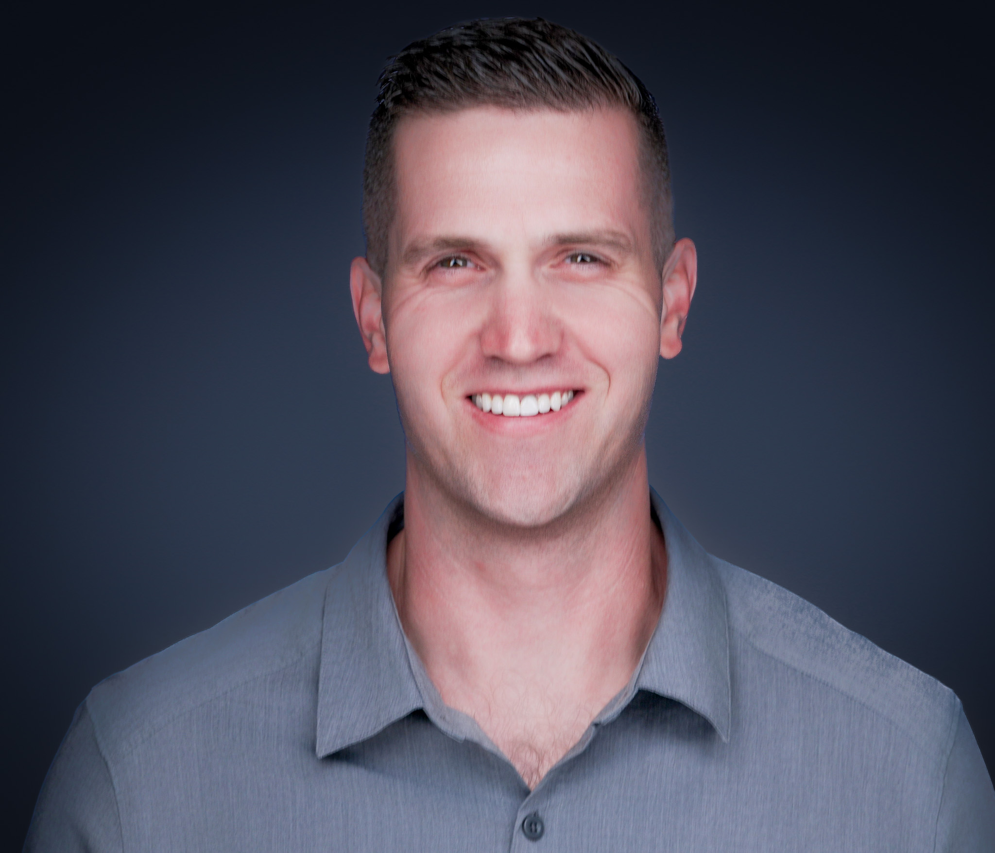 Smiling man in a gray polo shirt, studio headshot against a dark gray backdrop