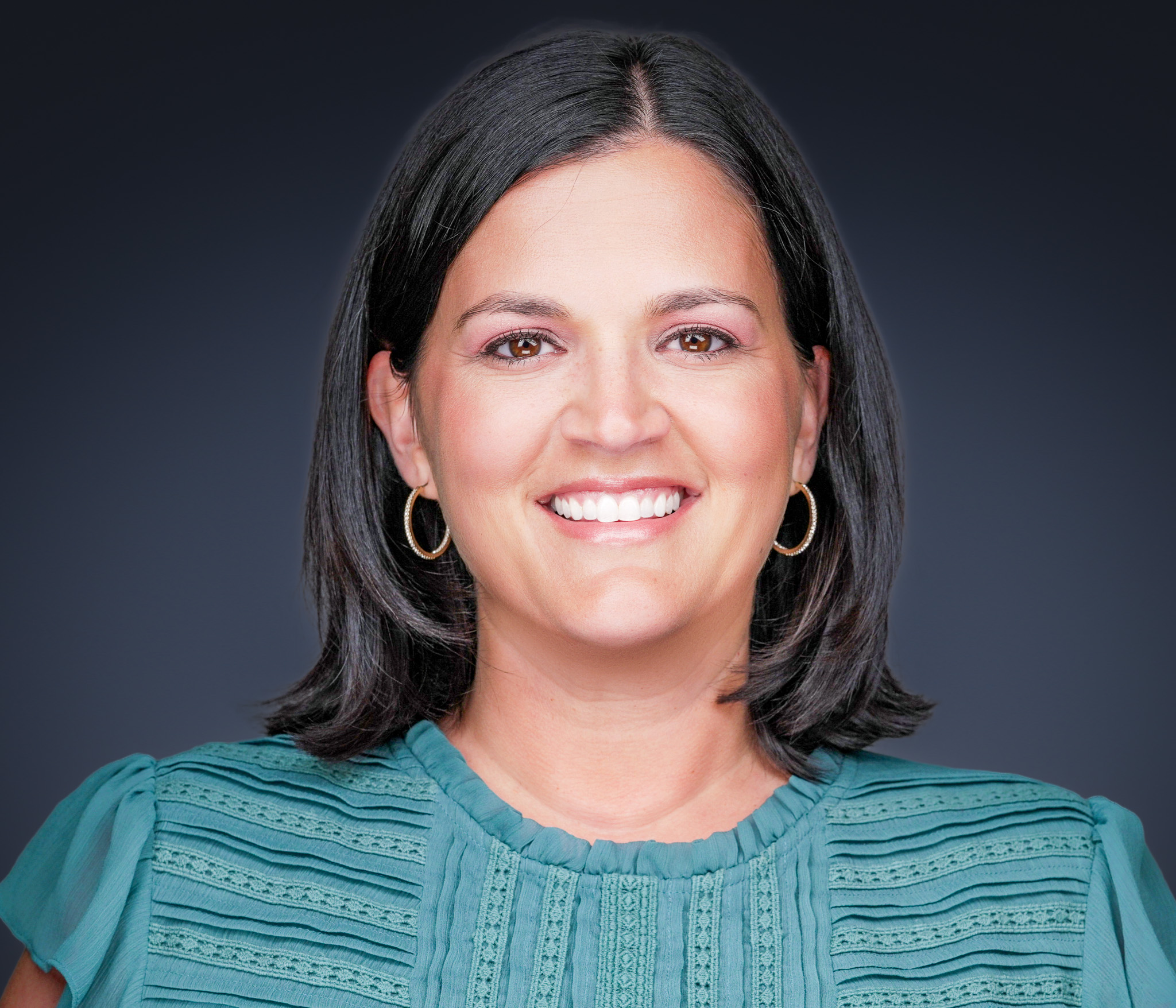 Smiling woman with dark hair in a teal knit top, studio headshot against a dark backdrop