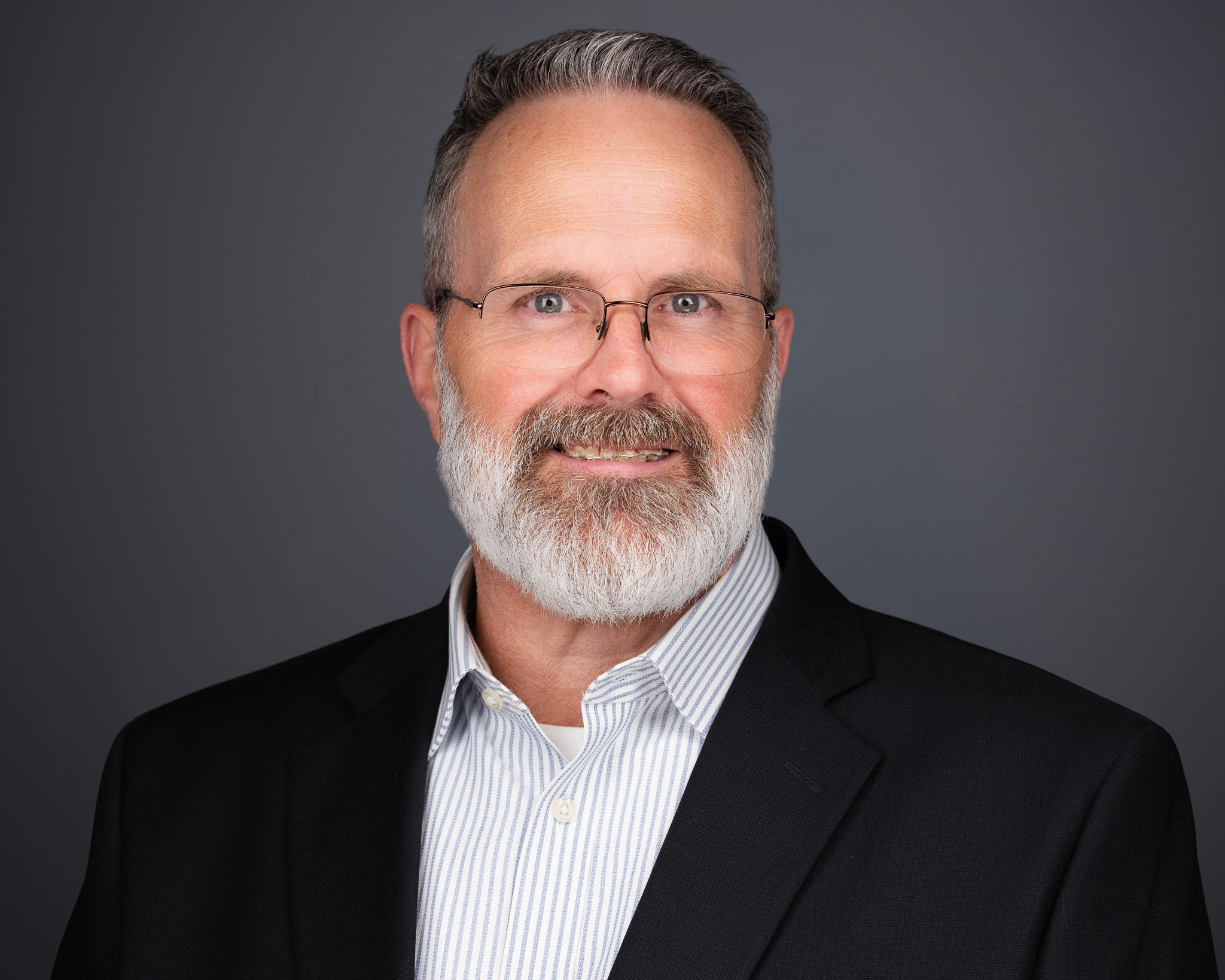 Man with a gray beard in a black blazer, studio headshot against a dark gray backdrop