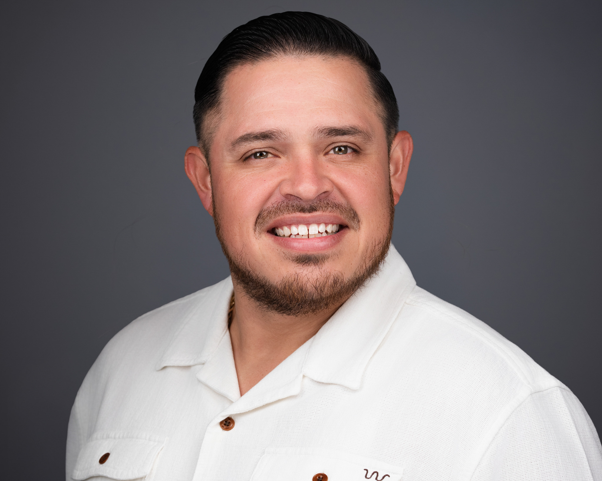 Smiling man in a white shirt, studio headshot against a dark gray backdrop