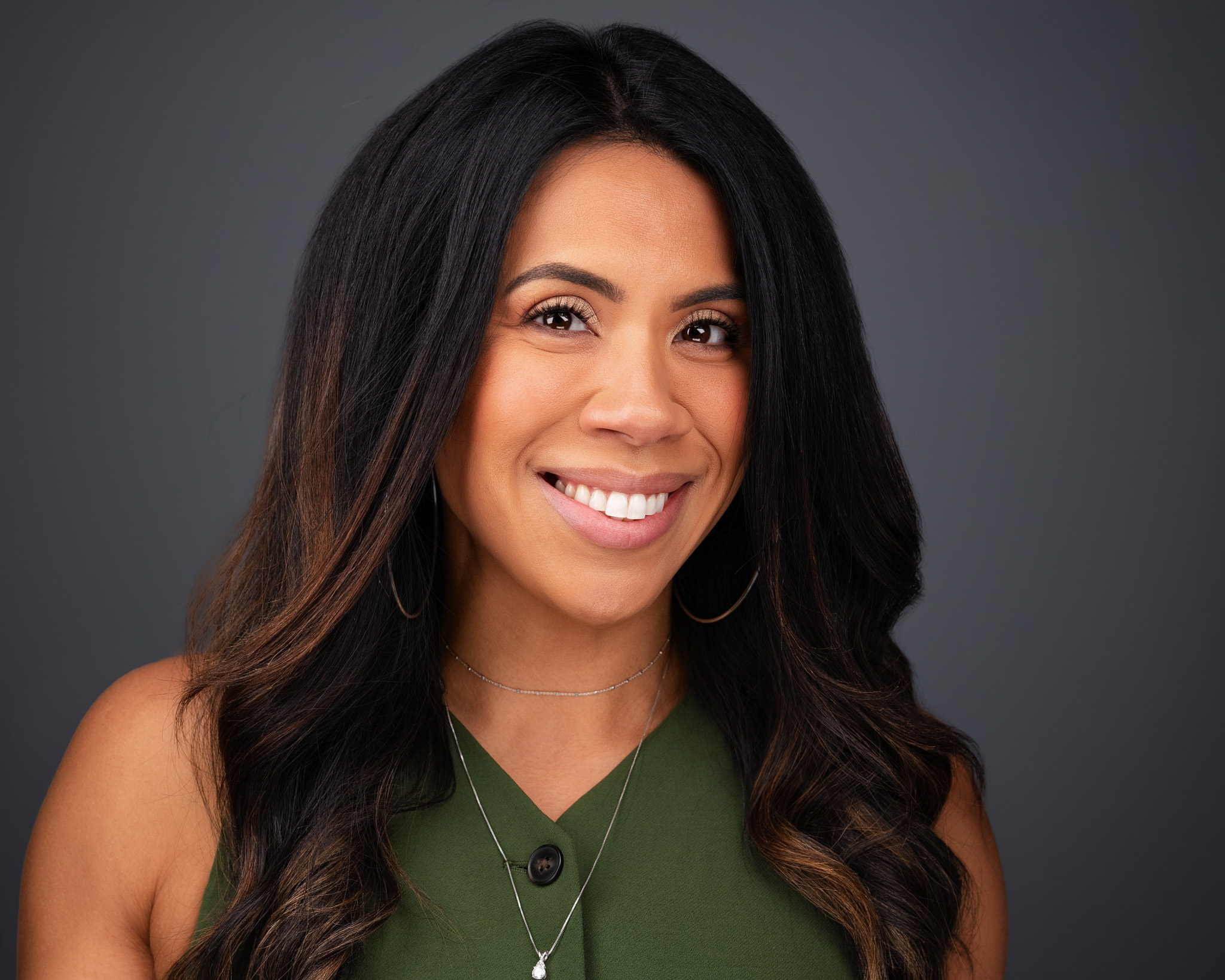Smiling woman with long dark hair in a green top, studio headshot against a dark gray backdrop