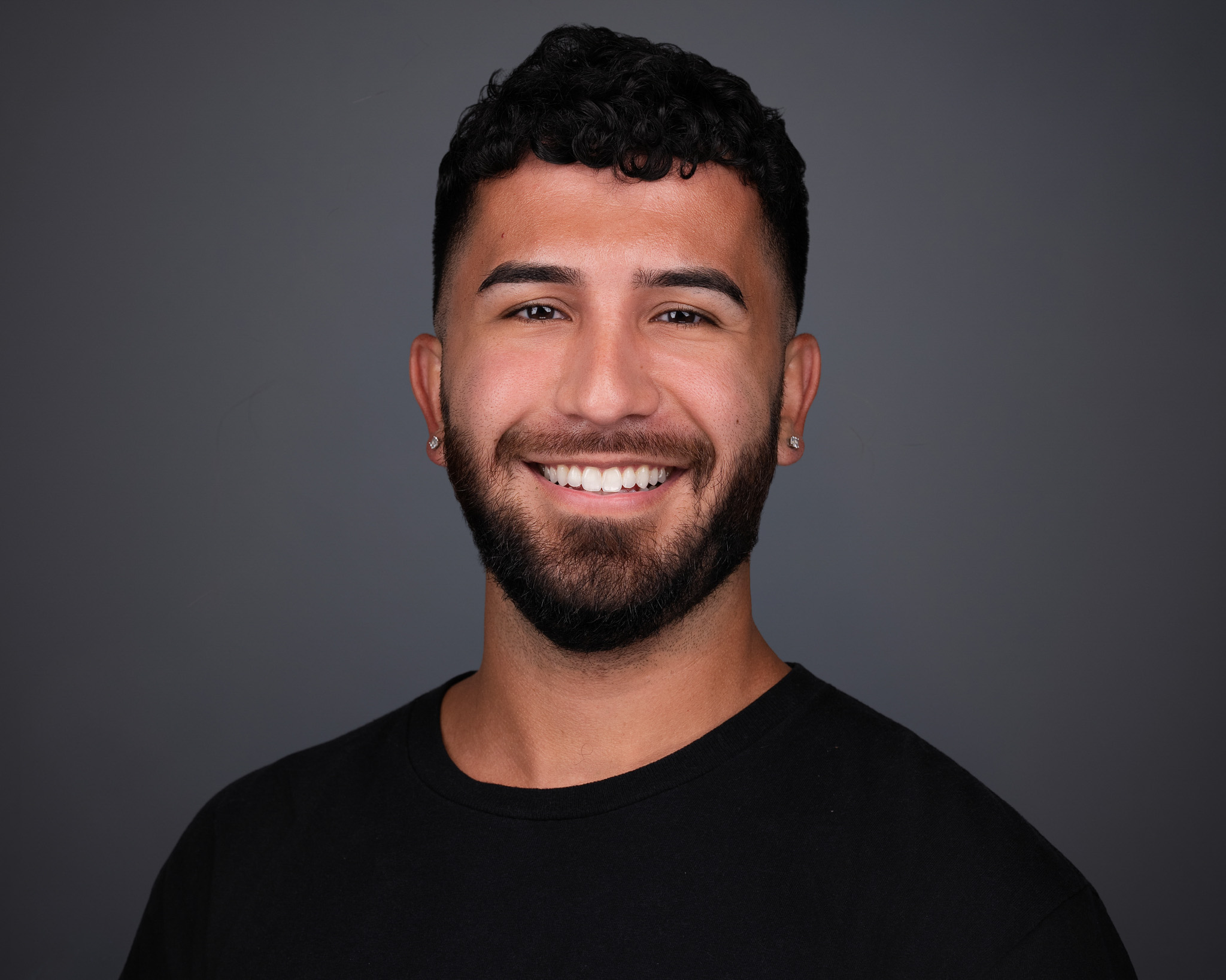 Smiling man with a short beard in a black t-shirt, studio headshot against a dark gray backdrop