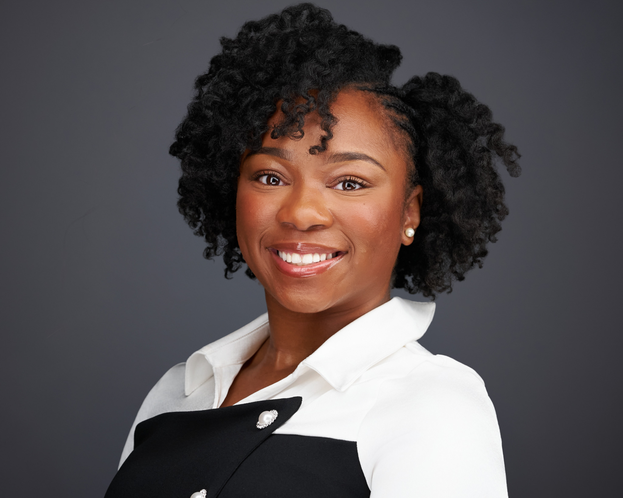 Smiling woman with curly dark hair in a black and white top, studio headshot against a dark gray backdrop