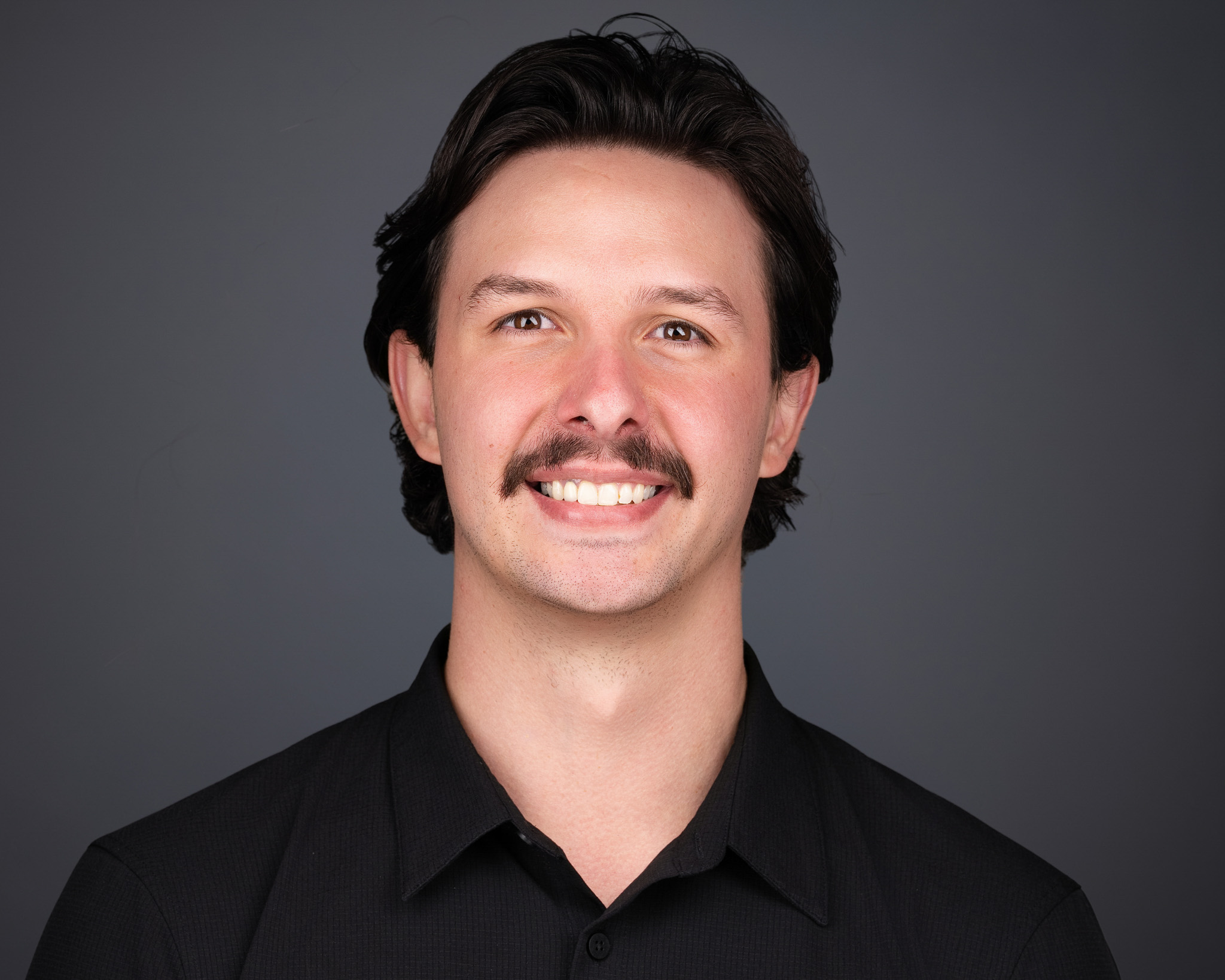 Man with a mustache in a black shirt, studio headshot against a dark gray backdrop