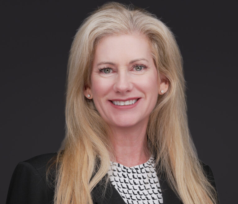Professional headshot of a smiling woman with long blonde hair wearing a black blazer