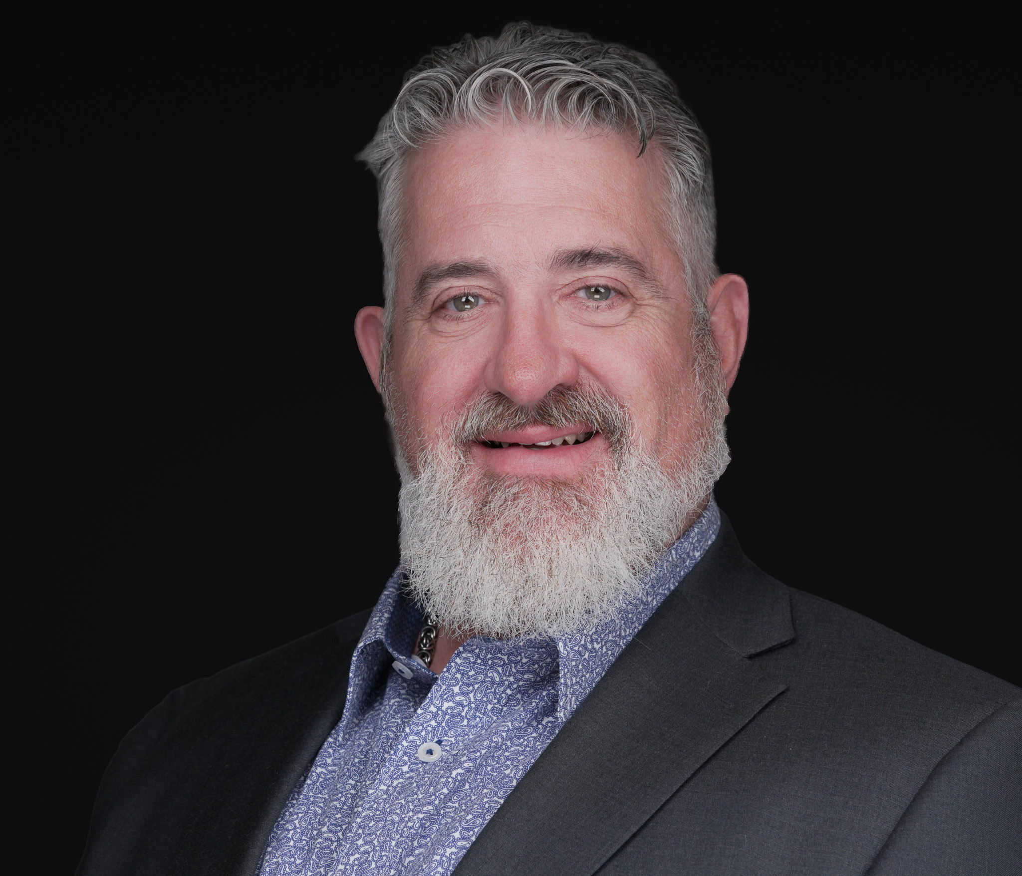 Man with a gray beard in a gray blazer, studio headshot against a dark gray backdrop