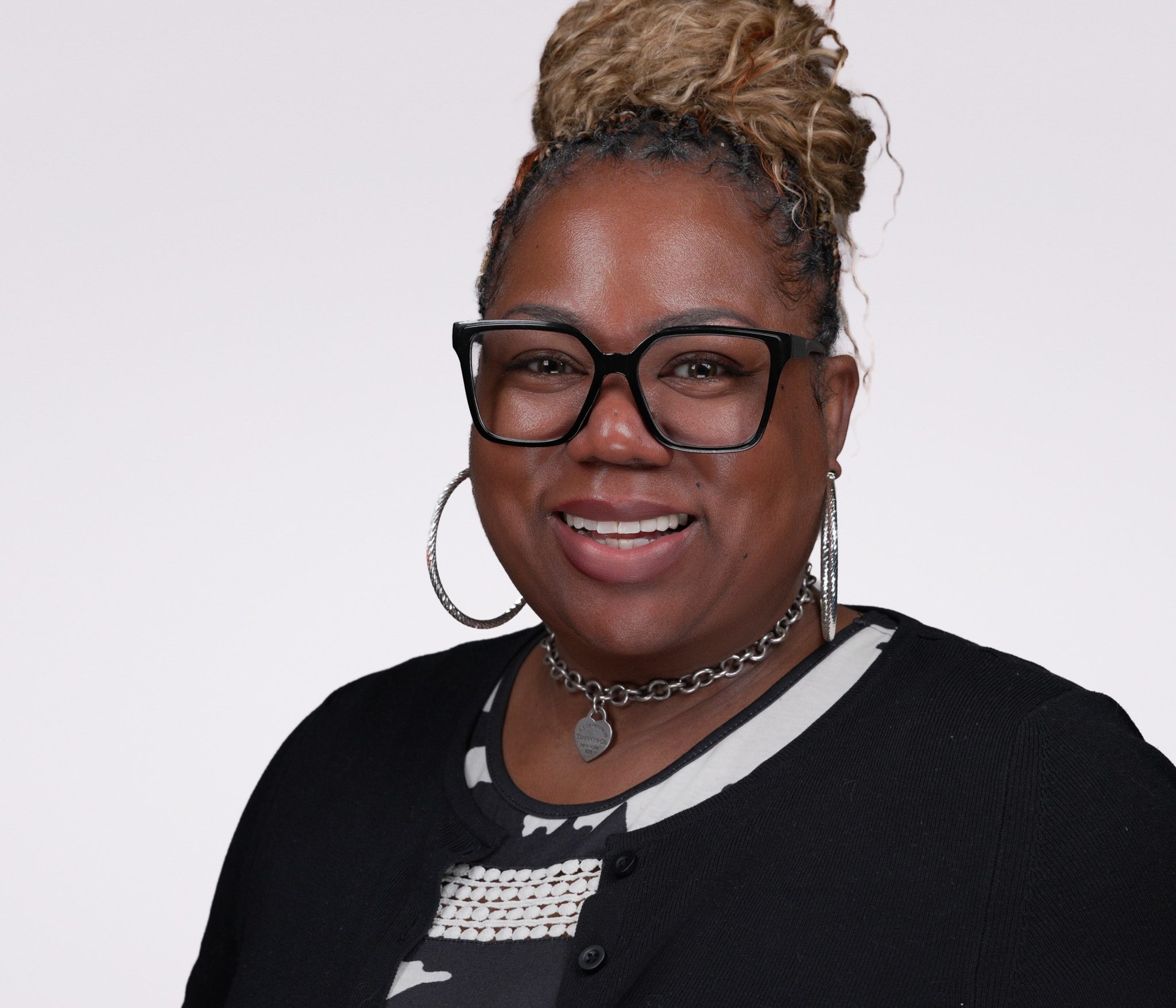 Smiling woman with braids and glasses in a black top, studio headshot against a white backdrop