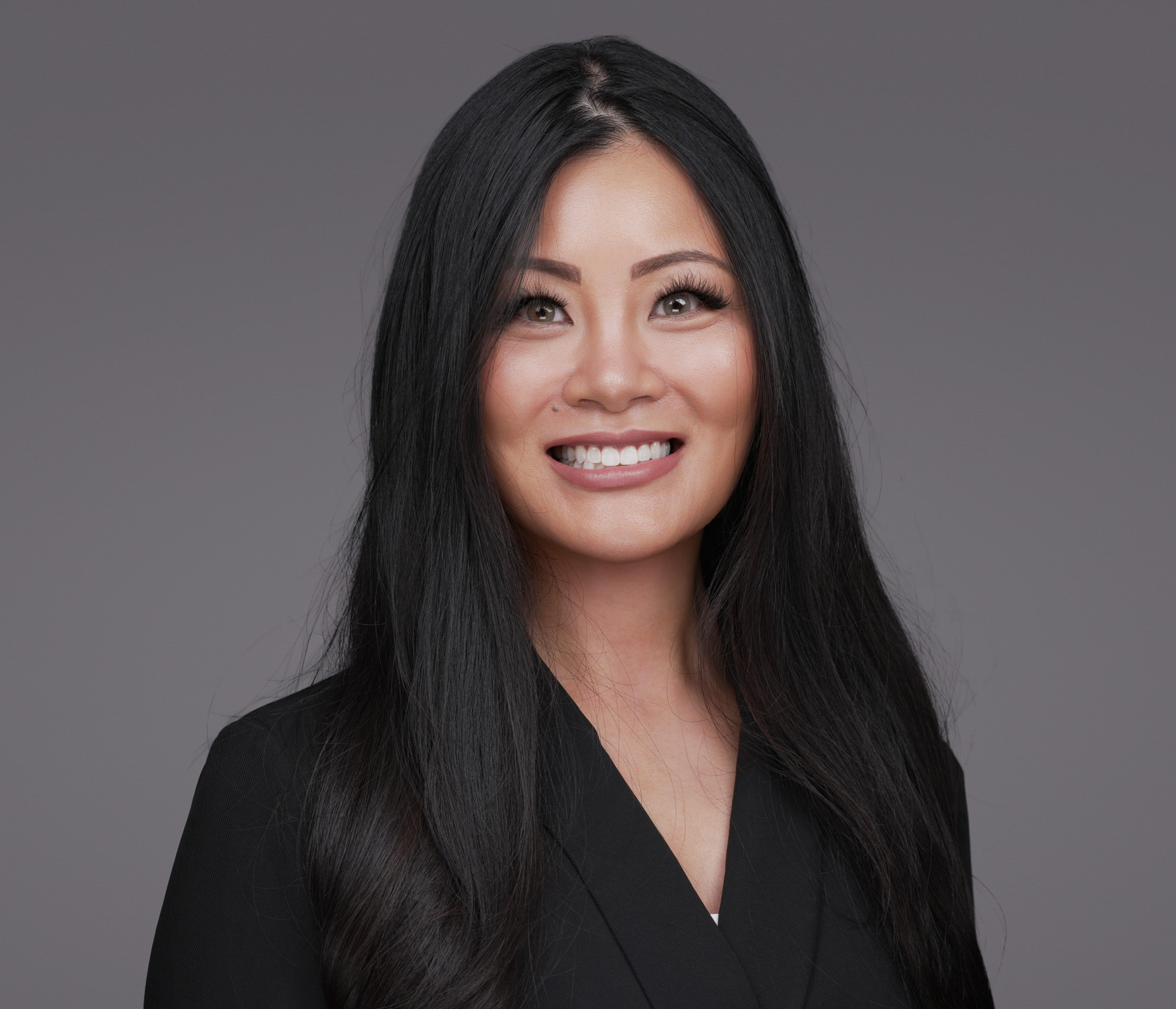 Woman with long black hair in a black top, studio headshot against a dark gray backdrop